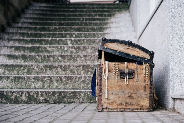 Treasure box by stairs that is partially open with jewelry hanging out