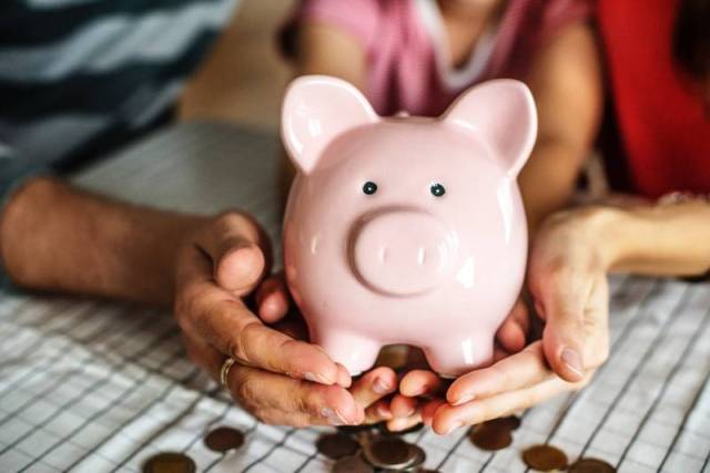 Family holding up a piggy bank with coins below it to represent their emergency savings