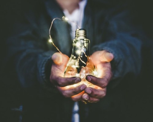 Man wearing business suit with hands cupped holding a lit lightbult