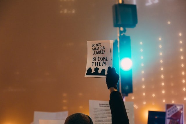 Man holding up a piece of paper that says "do not wait for leaders, become them."